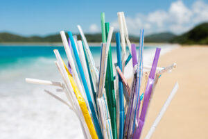 Heap of used plastic straws on background of clean beach and ocean waves