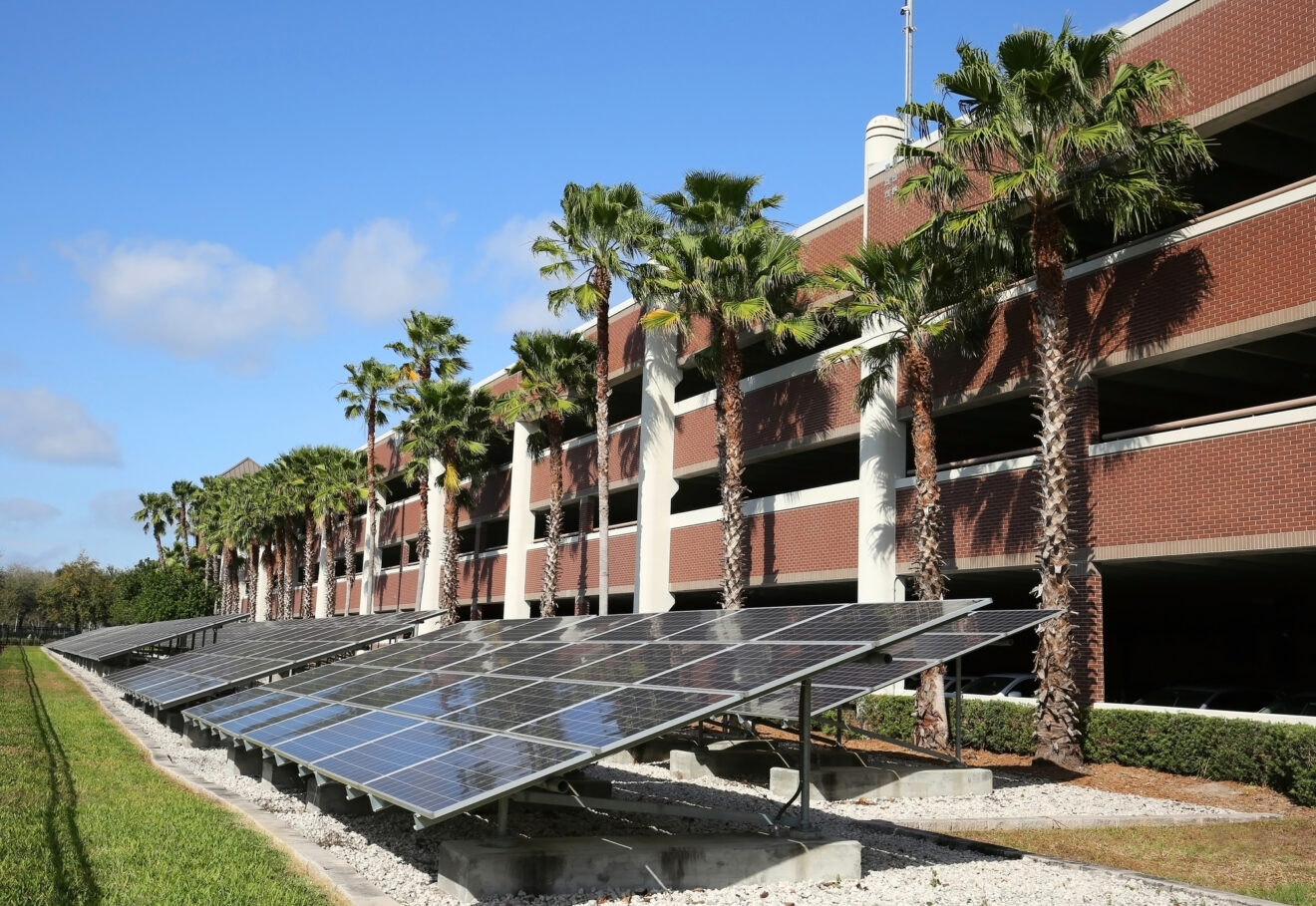Long line of solar panels converting the sun's rays into electricity in front of a parking garage.