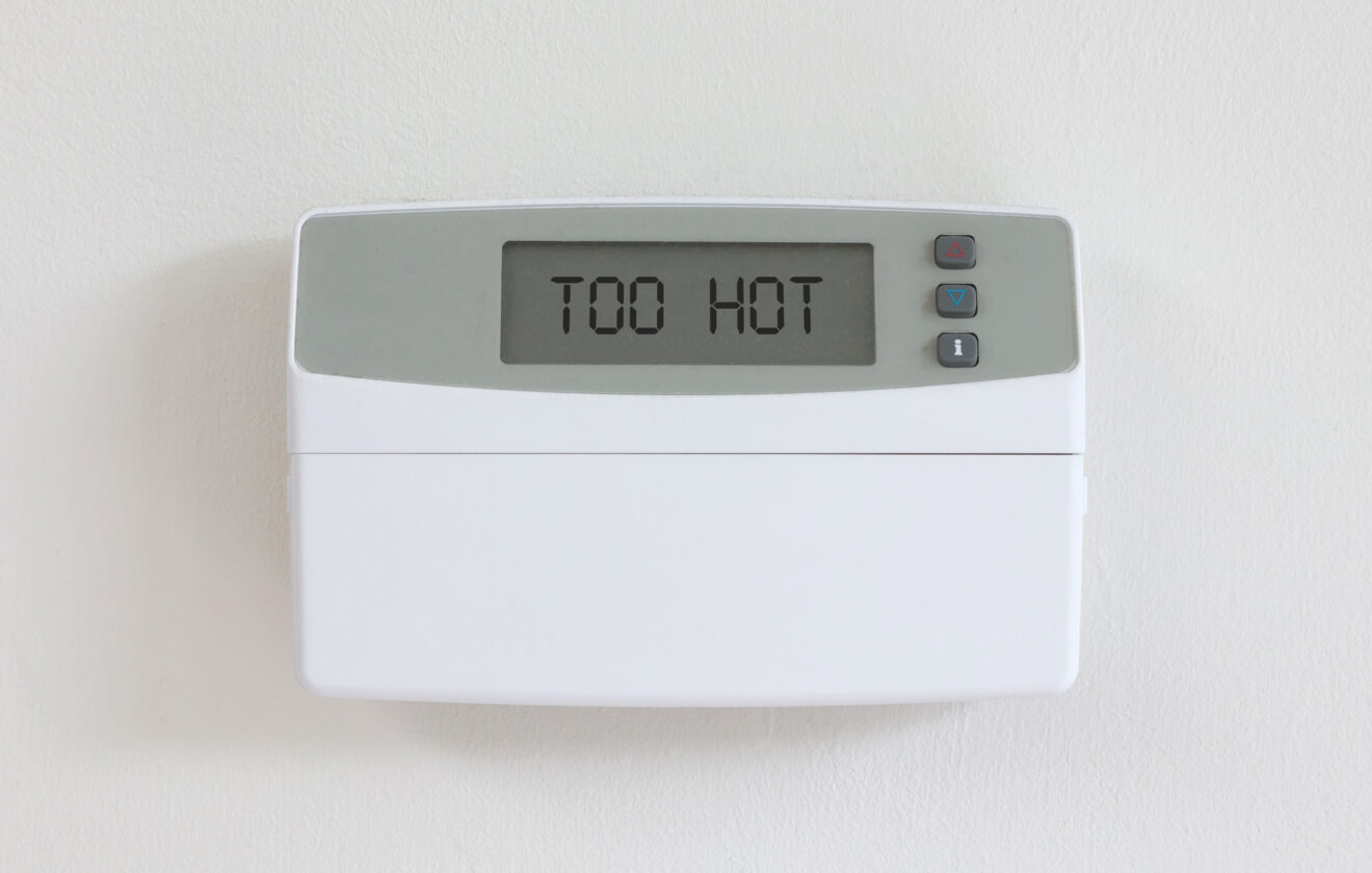 Vintage digital thermostat hanging on a white wall displaying "Too hot"