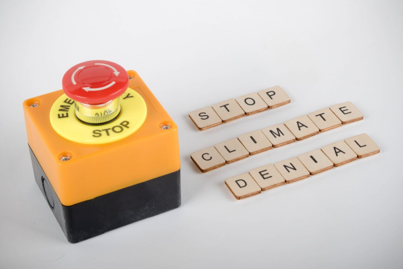 An industrial emergency stop button with a sign reading Stop Climate Denial
