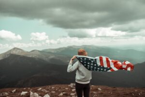 A woman holding USA flag on top of mountain